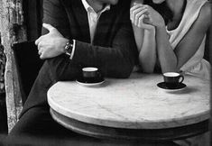 black and white photograph of two people sitting at a table with coffee cups on it