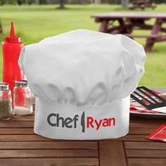 a white chef hat sitting on top of a wooden table next to utensils