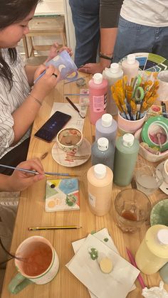 two women sitting at a table with craft supplies on it and one woman using scissors