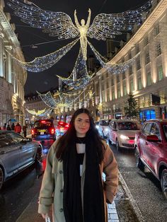 a woman standing in the middle of a busy street with christmas lights strung all around her