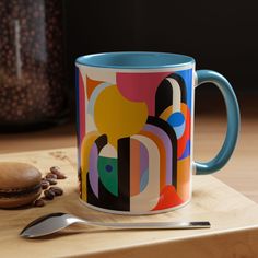 a colorful coffee mug sitting on top of a wooden cutting board next to a spoon