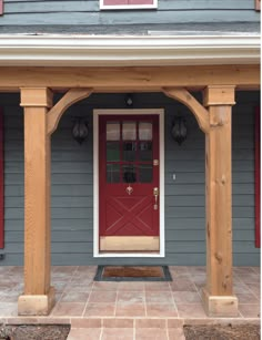 a red front door on a gray house with wooden pillars and arches over the entrance