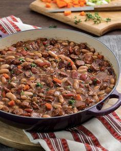 a pot filled with beans and carrots on top of a wooden table next to a cutting board