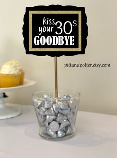 a cupcake on a stick in a glass bowl with herspooos and a sign that says kiss your 30's goodbye