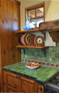 a bowl of fruit is on the counter in this kitchen with green tiles and wooden cabinets