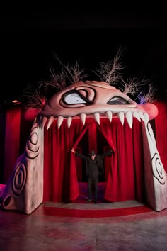 a man standing in front of a red curtain with an evil monster face on it