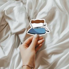 a hand holding a sticker with a coffee cup on it in front of white sheets