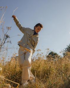 a man standing on top of a dry grass covered hillside next to tall grasses and trees