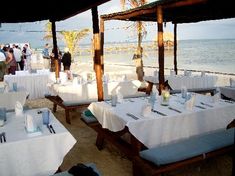 an outdoor dining area with white tablecloths and tables set up on the beach