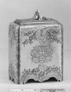 an antique silver box with ornate designs on the front and sides, next to a ruler