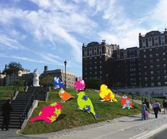 people walking on the sidewalk in front of some buildings with colorful kites flying above them