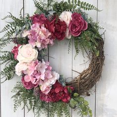 a wreath with pink and red flowers hanging on a wooden wall