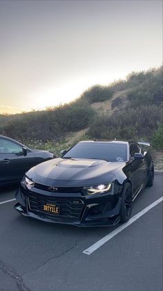 two cars parked in a parking lot next to each other with the sun setting behind them