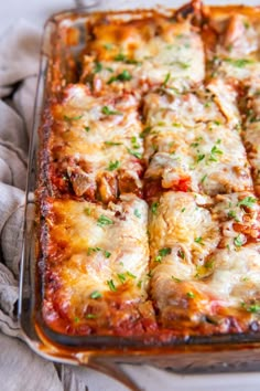 a casserole dish with meat, cheese and sauce in it on a cloth