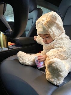 a baby sitting in the back seat of a car with a stuffed animal on it's arm