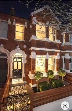 a large brick house with many windows and bushes in the front yard at night time