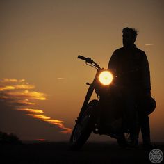 a man standing next to his motorcycle with the sun setting in the background and some words written on it