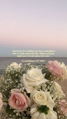 a vase filled with white and pink flowers next to the ocean