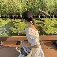 a woman in a white dress standing next to a river filled with water lilies