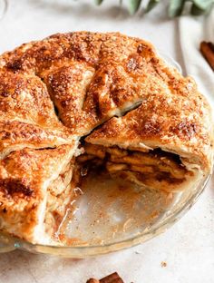 an apple pie is cut in half on a glass plate with cinnamon sticks around it