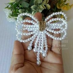 a hand holding a white beaded butterfly brooch with pearls on it's wings