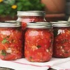 four jars filled with tomatoes sitting on top of a table