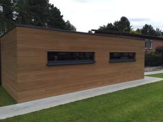 a wooden building sitting on top of a lush green field next to a sidewalk and trees