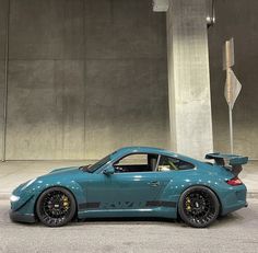 a blue sports car parked in front of a tall building with concrete floors and walls