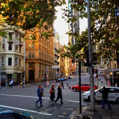 people crossing the street at an intersection on a sunny day with tall buildings in the background