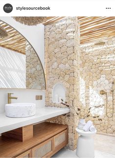 a bathroom with stone walls and flooring next to a wooden counter top under a round mirror