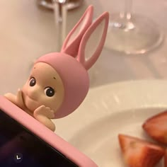 a small toy rabbit sitting on top of a cell phone next to strawberries and wine glasses