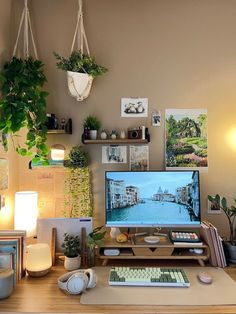 a desk with a computer monitor, keyboard and headphones on it in front of some plants