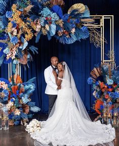 a bride and groom standing in front of a wedding arch with blue floral decorations on it