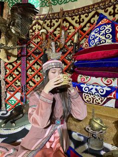 a woman sitting in front of a pile of rugs with an eagle on top of her head