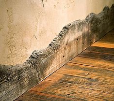 the corner of a room with wood flooring and peeling paint on it's walls