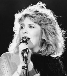 a black and white photo of a woman holding a microphone in her right hand while singing