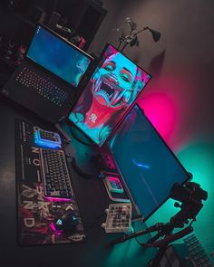 a desk with two laptops, a keyboard and a monitor on it in the dark