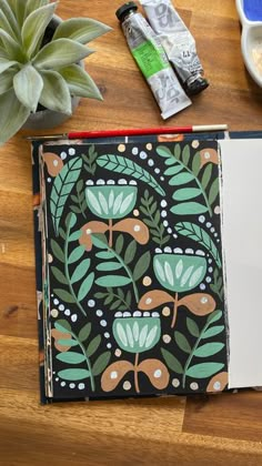 an open notebook sitting on top of a wooden table next to a potted plant