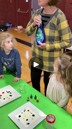 a woman standing in front of a table filled with kids and an adult holding a bottle