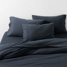 the bed is made with dark blue sheets and pillowcases, along with two pillows