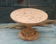 an old wooden cake stand sitting on top of a blue tablecloth covered floor next to some dried grass