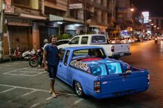 a man standing next to a blue truck in the middle of a street at night