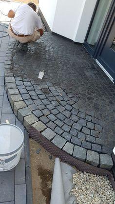 a man laying bricks on the ground next to a white bucket and cement pavers