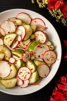 a white bowl filled with sliced radishes on top of a table next to red flowers