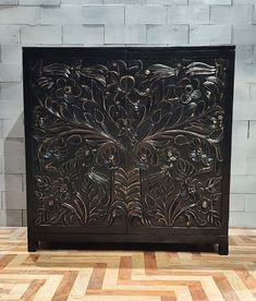 an ornate wooden cabinet with flowers and leaves on it's side, against a brick wall