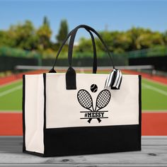 a black and white tote bag with a tennis racket design on it sitting on a wooden table