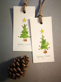 two christmas cards hanging from twine with pine cone on the bottom one has a drawing of a tree