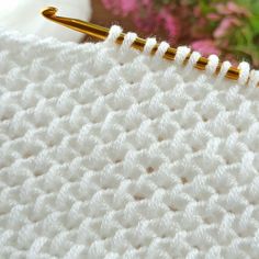 a close up view of a crochet stitch on a white blanket with flowers in the background