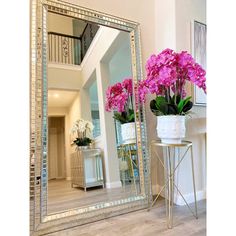 a large mirror sitting on top of a wooden floor next to a vase filled with flowers