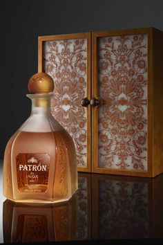 a bottle of patron on a reflective surface next to a wooden box with an ornate design